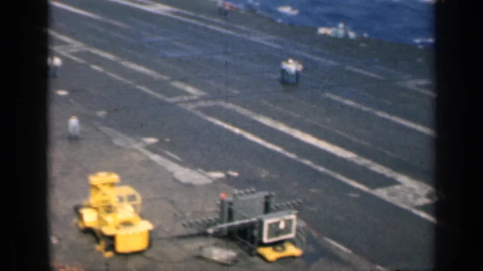 Closer view of the carrier deck with yellow deck vehicle, white landing markings, and scattered crew figures during the 1962 Cuba metadata sequence.