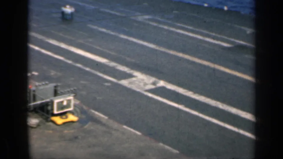 Aircraft carrier deck area with white markings, yellow equipment, and visible 8mm frame borders, continuing the at-sea naval view.