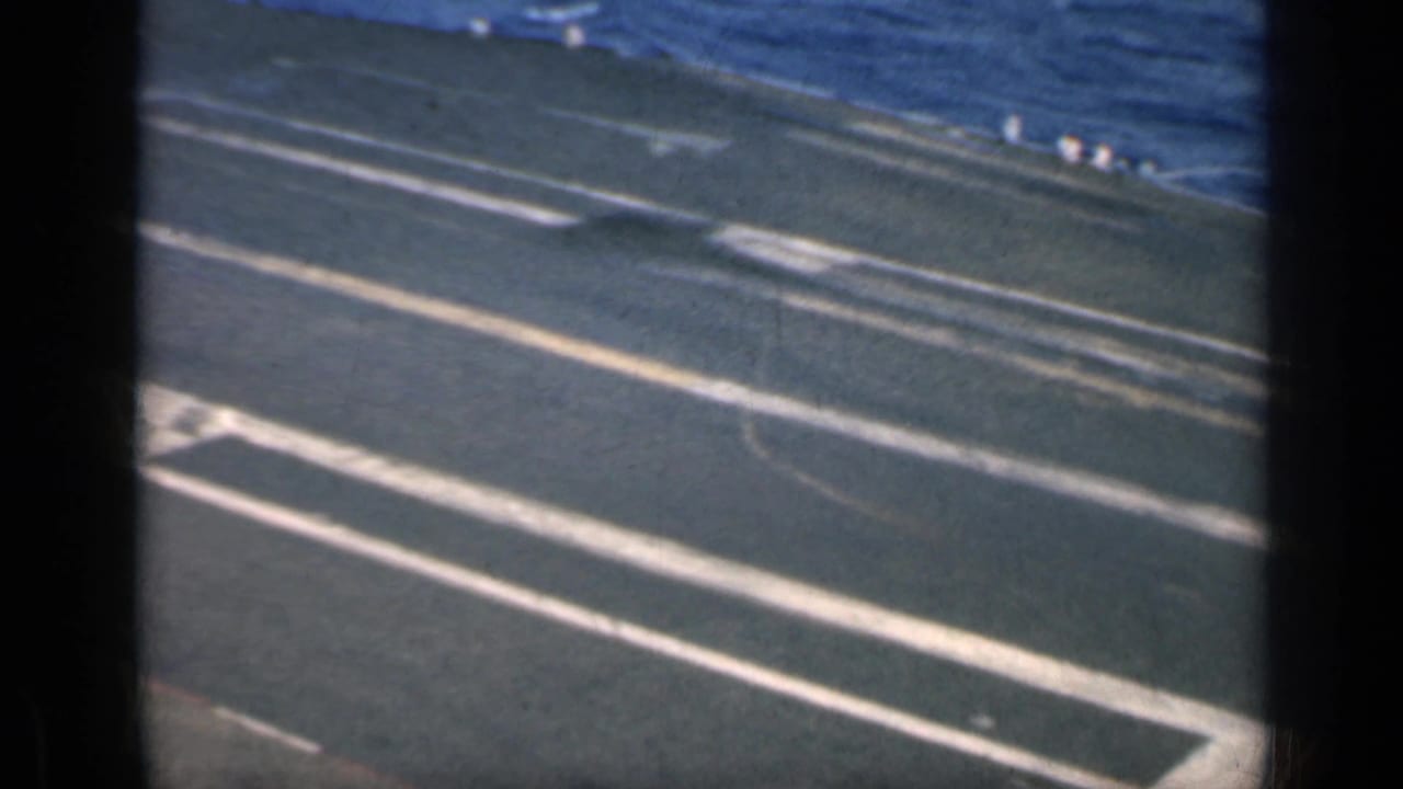 High-angle view of a carrier deck with ocean beyond and painted runway markings.