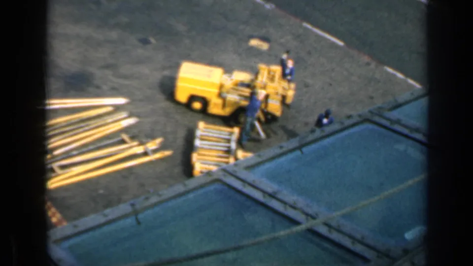 Elevated 1962 Cuba view of workers beside yellow construction machinery and metal beams in bright daylight.