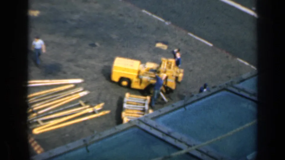 High-angle 8mm frame from Cuba in 1962 showing workers near a yellow machine and construction materials.