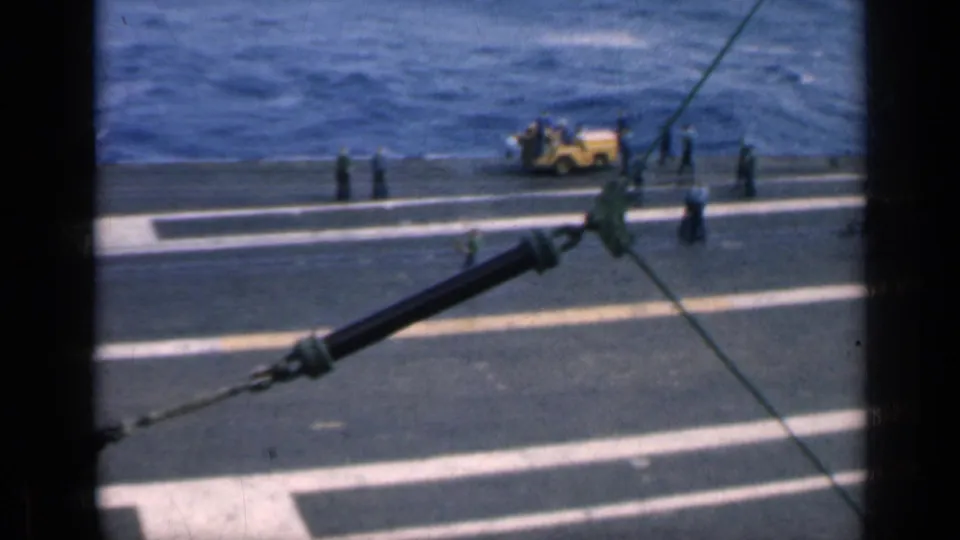 The deck of a vessel borders blue water, with workers, rigging lines, and a yellow machine visible in 1962 Cuba footage.