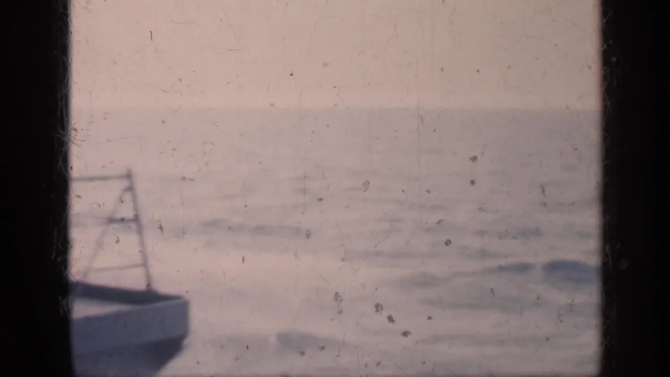 Faded 8mm frame looking from the carrier toward open water, with ship structure at the lower edge and sea filling the background.