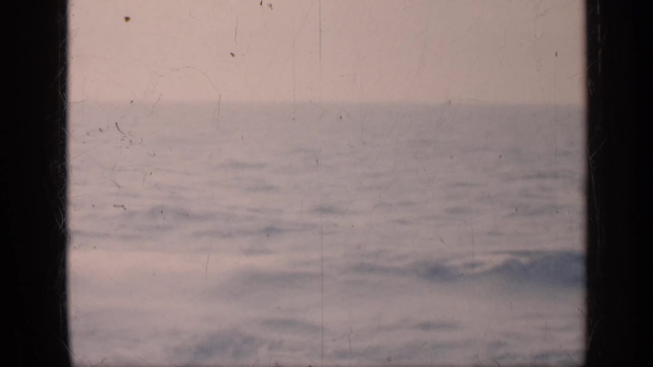 Open ocean under a pale sky, seen through dark vertical frame edges.