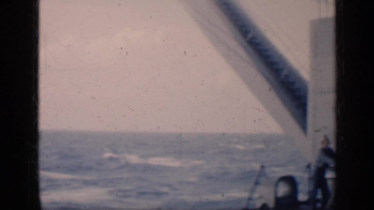 1962 Cuba travel footage appears to show open water from a moving ship, framed by dark film edges and a diagonal deck structure.