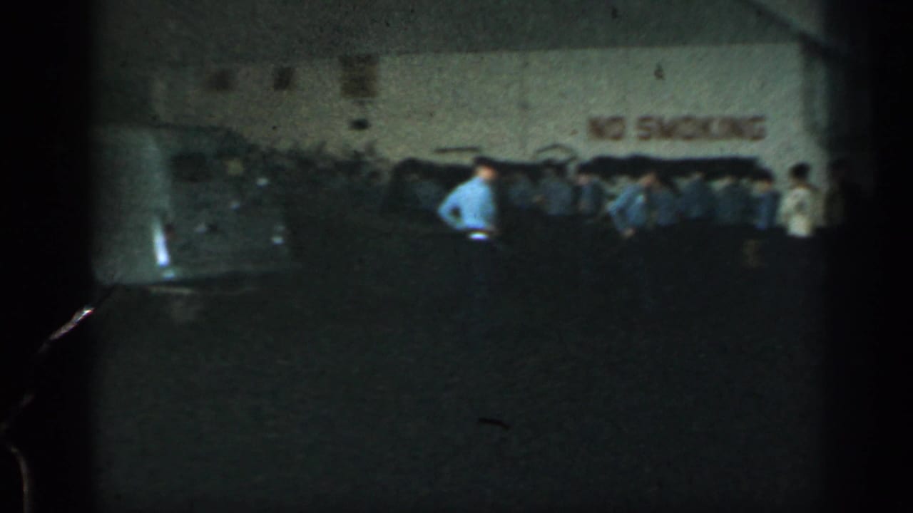 Workers stand in a dim warehouse near a wall with a no-smoking notice.