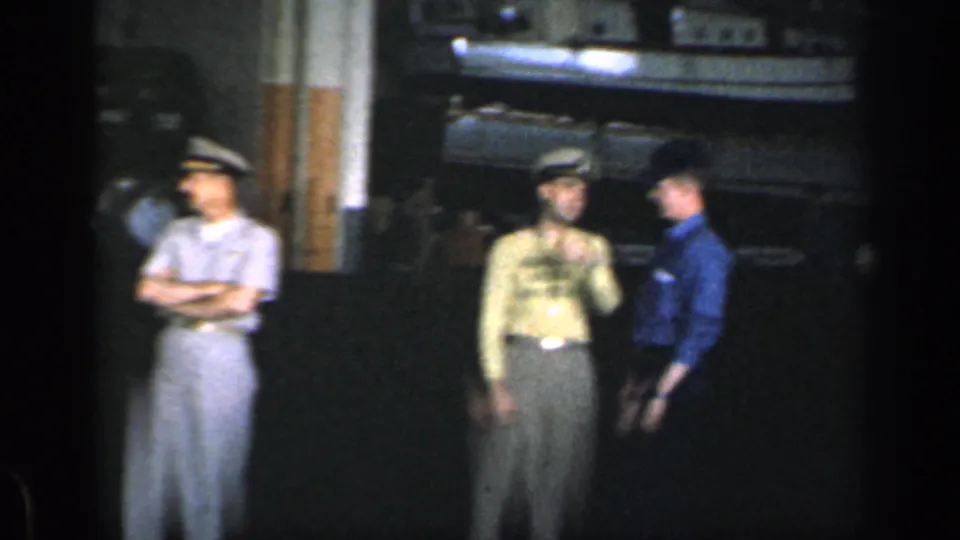 Three uniformed men stand in a dim Cuban warehouse beside what appears to be a truck or loading area.