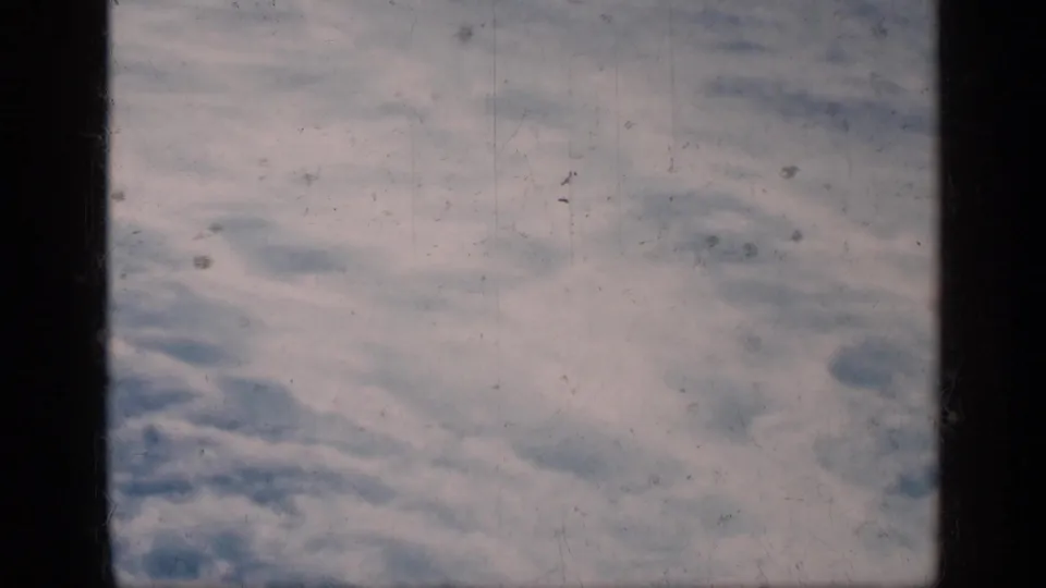 Open sea and sky are viewed through dark ship window framing in grainy 1960s 8mm footage.