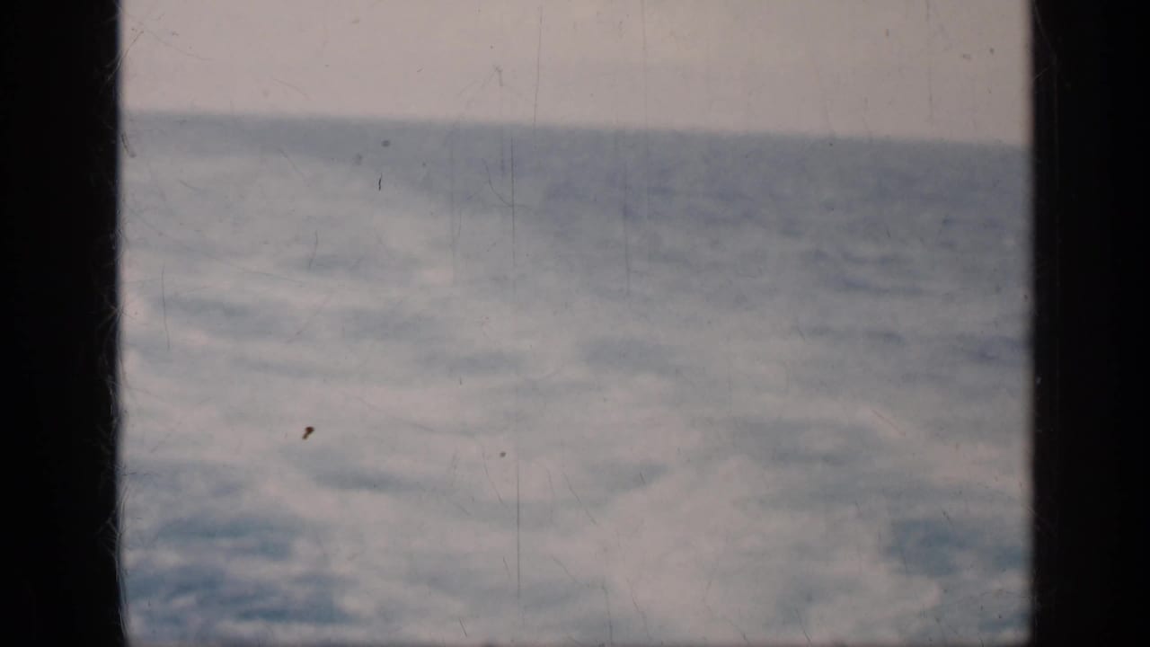 Rough blue sea and cloudy sky seen through dark vertical window framing.