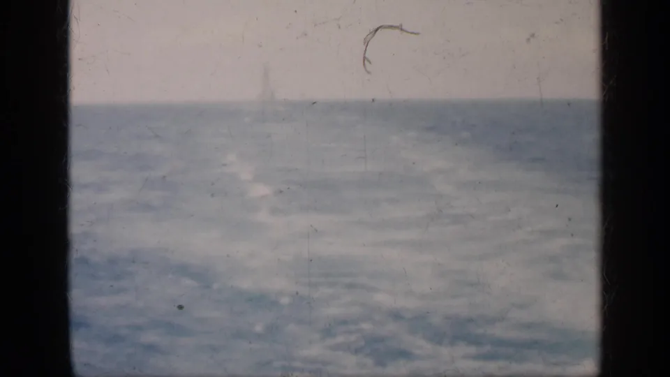 1962 Cuba 8mm frame showing turbulent sea, faint whitecaps, cloudy sky, and a dark window divider in the foreground.