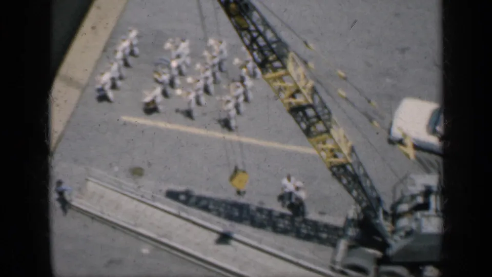1962 Cuba elevated 8mm frame showing a crane, uniformed group, paved markings, rail-like structures, and a white vehicle.