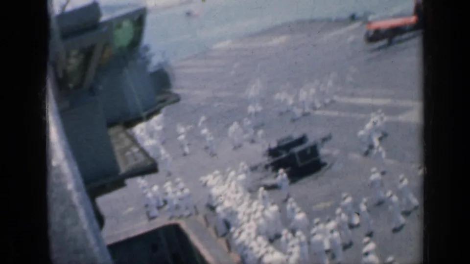 Cuba-linked 1962 8mm frame looking down at sailors in white organized across a carrier deck beside ship structures.
