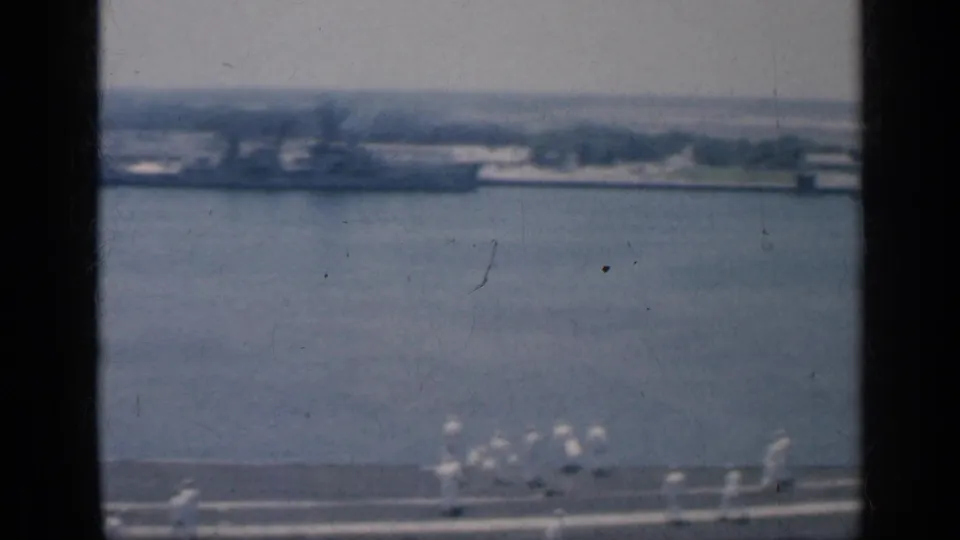 Shipboard view across a Cuban harbor, framed by window bars with distant buildings and deck detail below.
