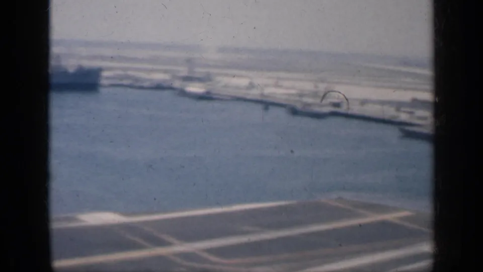 Final shipboard view of a Cuban harbor, with deck markings below, shoreline structures beyond, and heavy window framing.