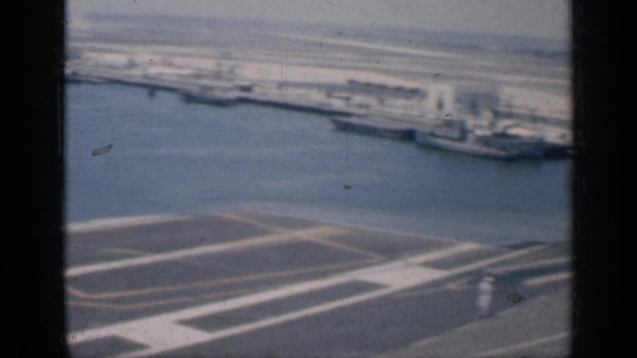 1962 Cuba harbor view from an aircraft carrier deck, with water, docked warships, and industrial shoreline beyond.