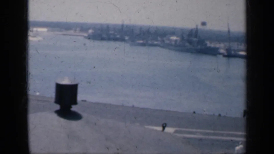 Soft 8mm view from an aircraft carrier deck toward Cuba harbor, with a deck fixture, water, shoreline, and moored vessels.