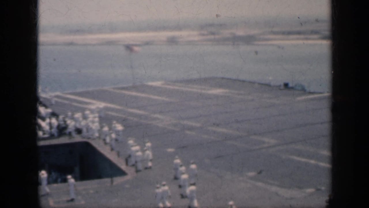1962 Cuba home-movie frame showing sailors grouped on an aircraft carrier deck beside harbor water and port structures.