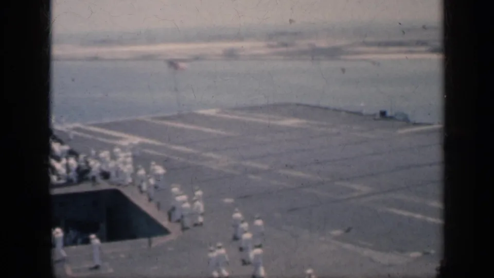 1962 Cuba home-movie frame showing sailors grouped on an aircraft carrier deck beside harbor water and port structures.