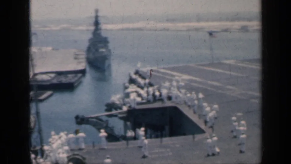 1962 Cuba frame with a naval vessel in harbor, sailors on the carrier deck, and dockside equipment in soft 8mm focus.
