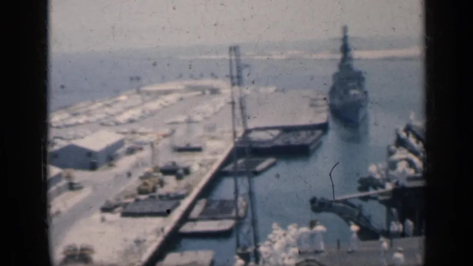 1962 Cuba home-movie view past carrier deck structures and cranes toward a naval vessel docked in the harbor.