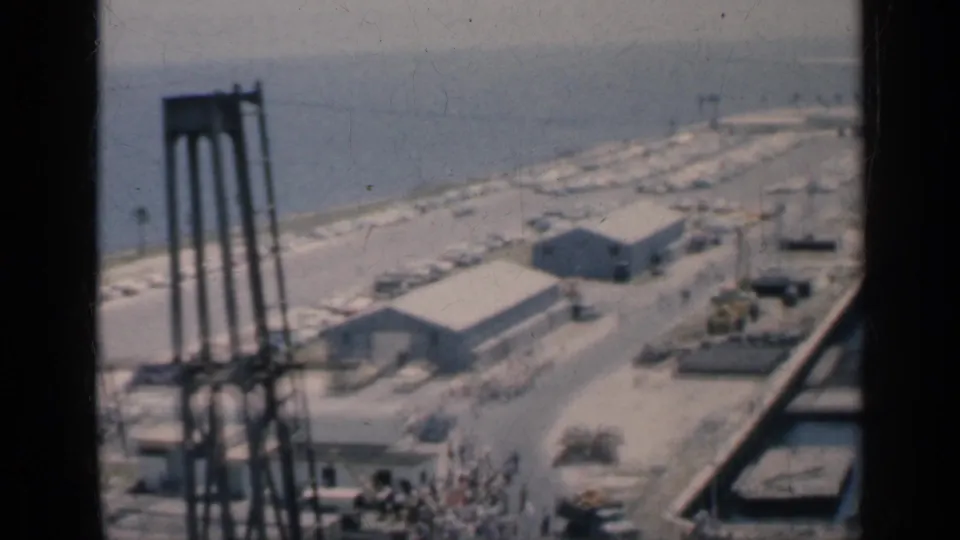 1962 Cuba port view showing dock buildings, tall crane structures, parked vehicles, shoreline, and harbor water through dark film-frame divisions.