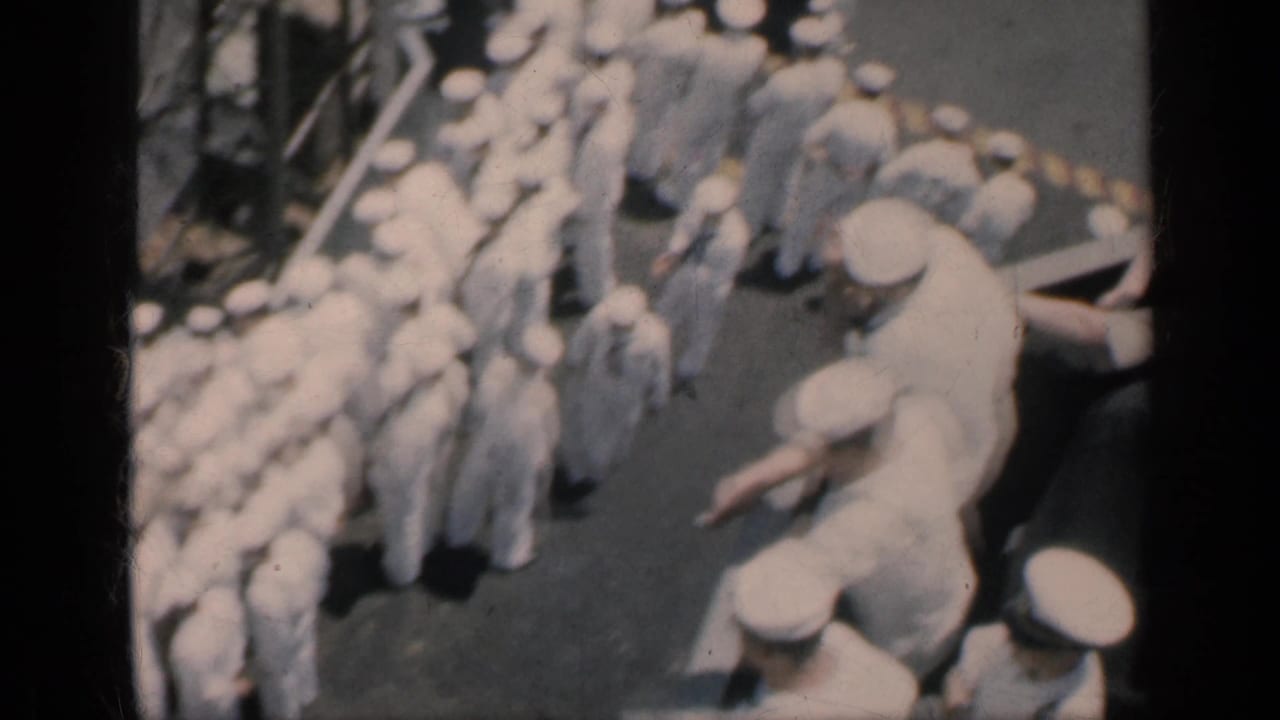 Sailors in white uniforms gathered closely on a ship deck.