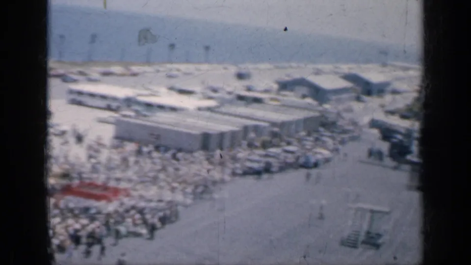 1962 Cuba 8mm frame with a wide elevated view of a coastal crowd, low buildings, beach sand, and the shoreline in the distance.