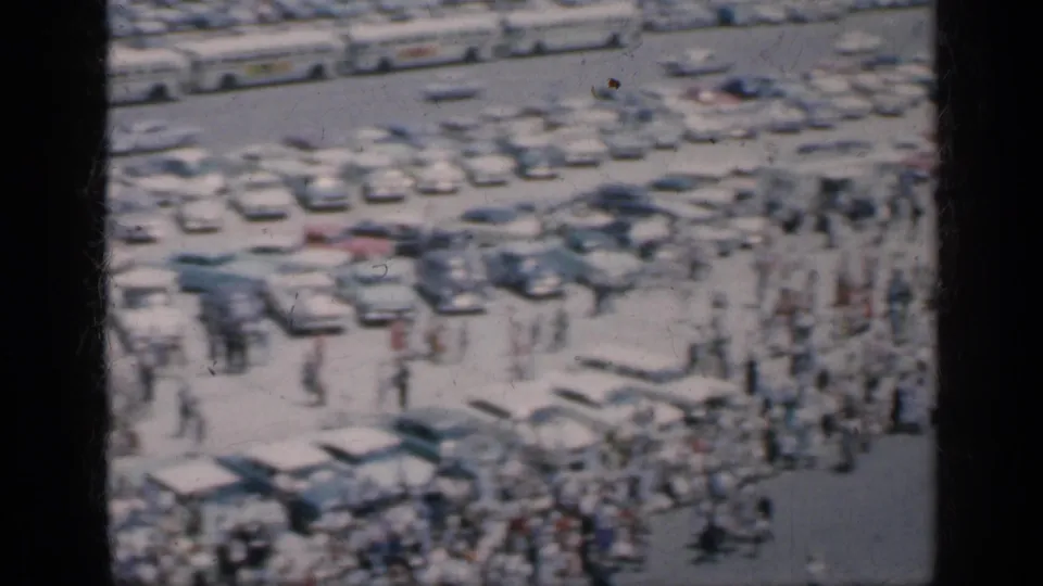Elevated 1962 Cuba view with rows of classic cars, pedestrians, and dense activity across an open paved area.