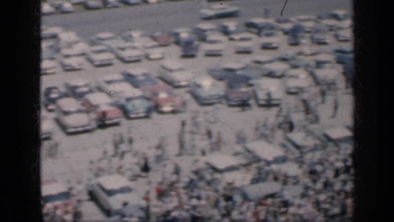 Soft 8mm frame from Cuba in 1962 showing people mingling around parked classic cars in a crowded outdoor setting.