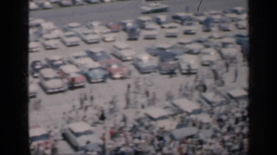 Soft 8mm frame from Cuba in 1962 showing people mingling around parked classic cars in a crowded outdoor setting.