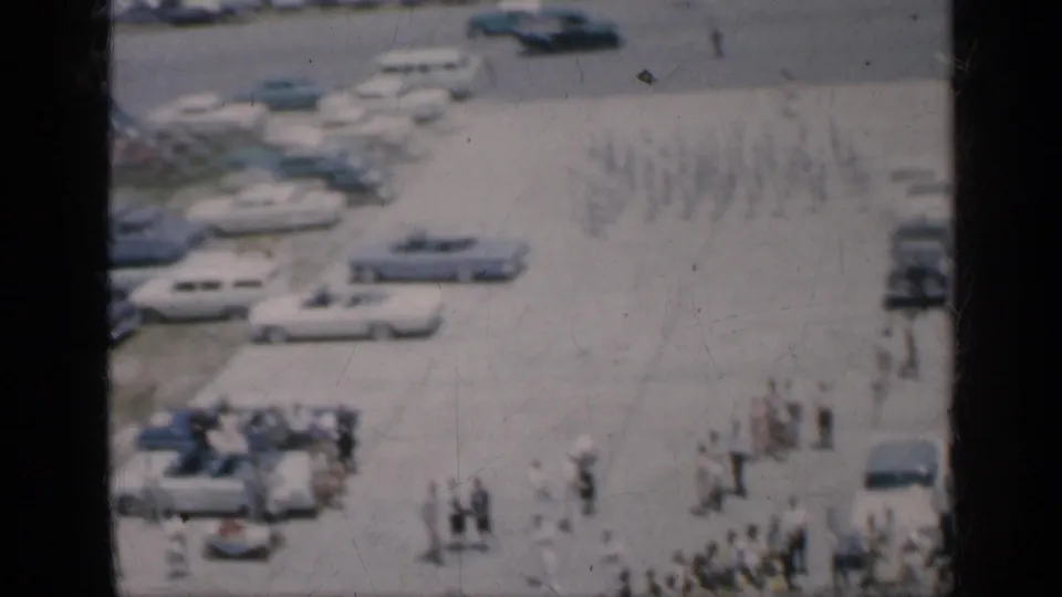 1962 Cuba 8mm frame showing an elevated view over parked cars, scattered people, and a waterfront area partly obscured by dark film edges.
