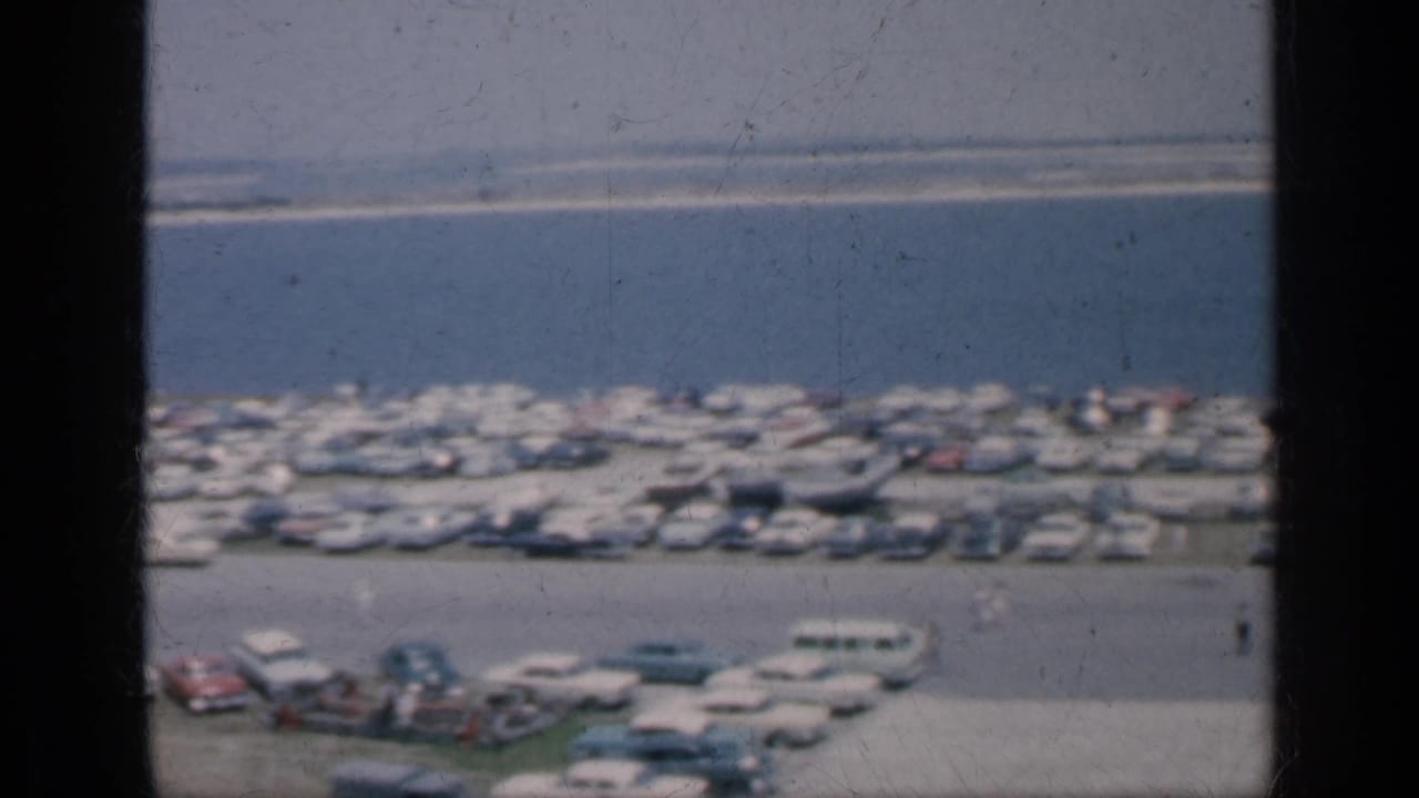 1962 Cuba 8mm frame with a soft elevated view of cars clustered near water, a few small figures, and visible film scratches.