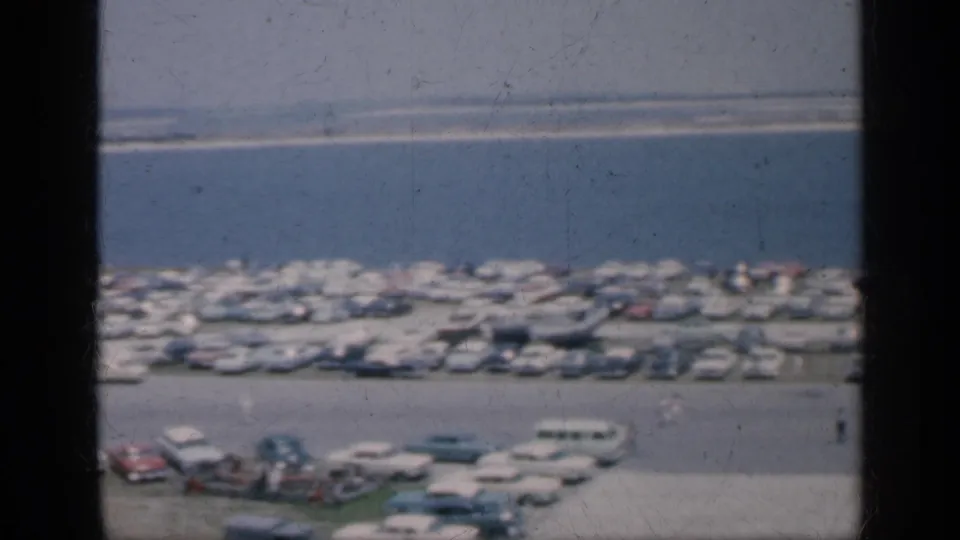 1962 Cuba 8mm frame with a soft elevated view of cars clustered near water, a few small figures, and visible film scratches.
