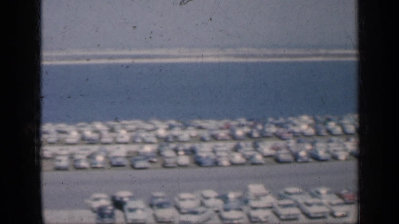Waterfront parking area seen through dark window bars with rows of cars and buses.