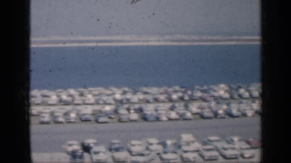 1962 Cuba 8mm view of a crowded waterfront parking area with parked cars, buses, sea horizon, and dark window framing.