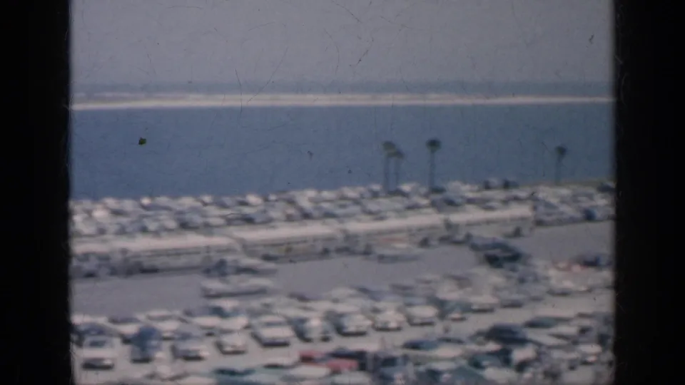 1962 Cuba 8mm frame of parked cars near a waterfront lined with palm trees, seen from behind dark window bars.