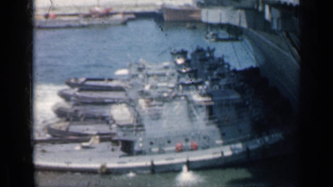 1962 Cuba 8mm frame showing harbor water, small boats, dock structures, and a distant gray ship from an elevated viewpoint.