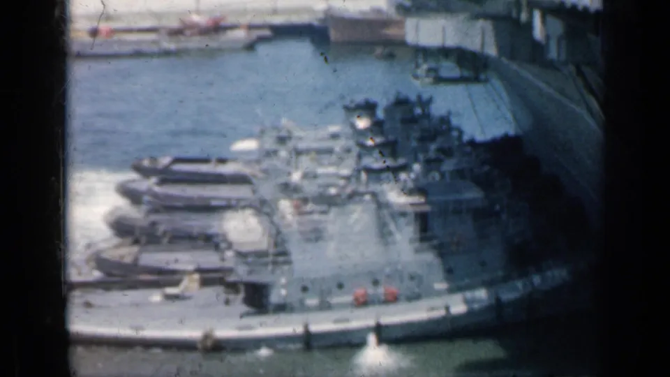 1962 Cuba 8mm frame showing harbor water, small boats, dock structures, and a distant gray ship from an elevated viewpoint.