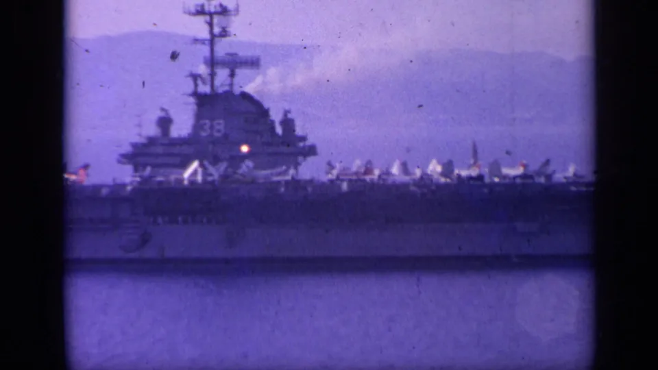 Italy-associated 1962 frame showing the carrier island, deck aircraft, and a partly visible hull number on the side of the ship.