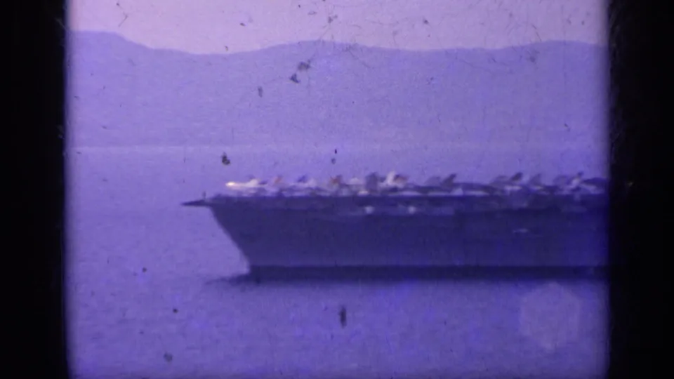 1962 Italy-associated home-movie frame showing the carrier bow and flight deck aircraft in soft purple-tinted 8mm footage.