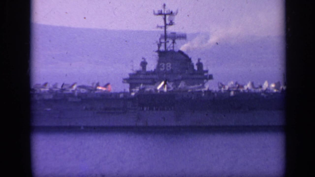 U.S. Navy aircraft carrier with hull number 38 on calm water near hazy mountains.