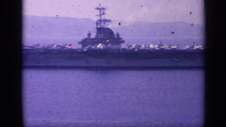 Closer 8mm view of the U.S. Navy carrier in 1962 Italy, showing the island structure, deck aircraft, and soft mountain background.