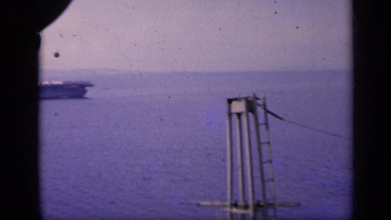 Open ocean seen through dark vertical framing with part of a carrier structure at left.