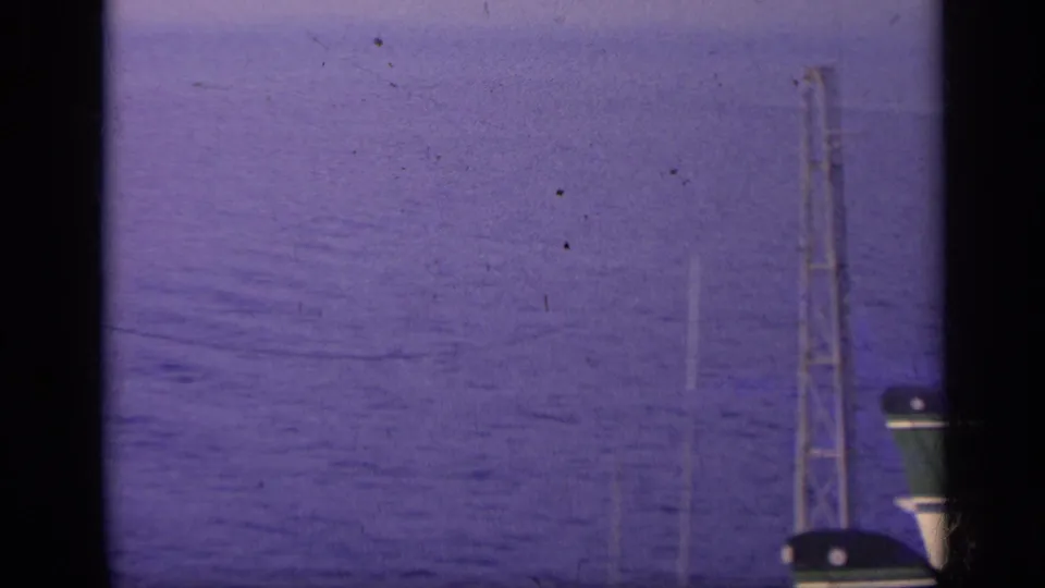 A carrier mast and rigging appear against the sea, partly blocked by dark vertical film or window framing in the 1962 Italy footage.