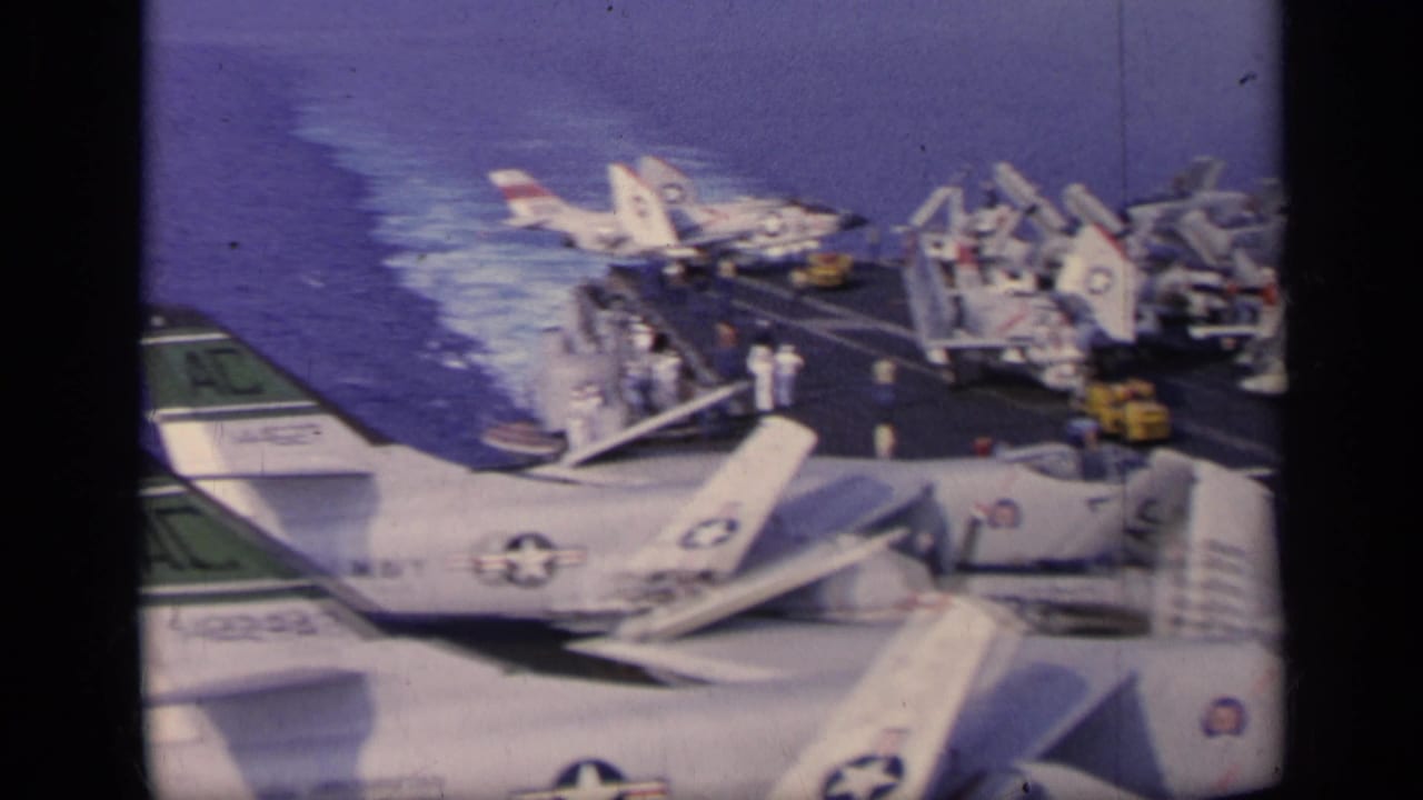 U.S. Navy aircraft parked on an aircraft carrier deck with ocean wake behind.