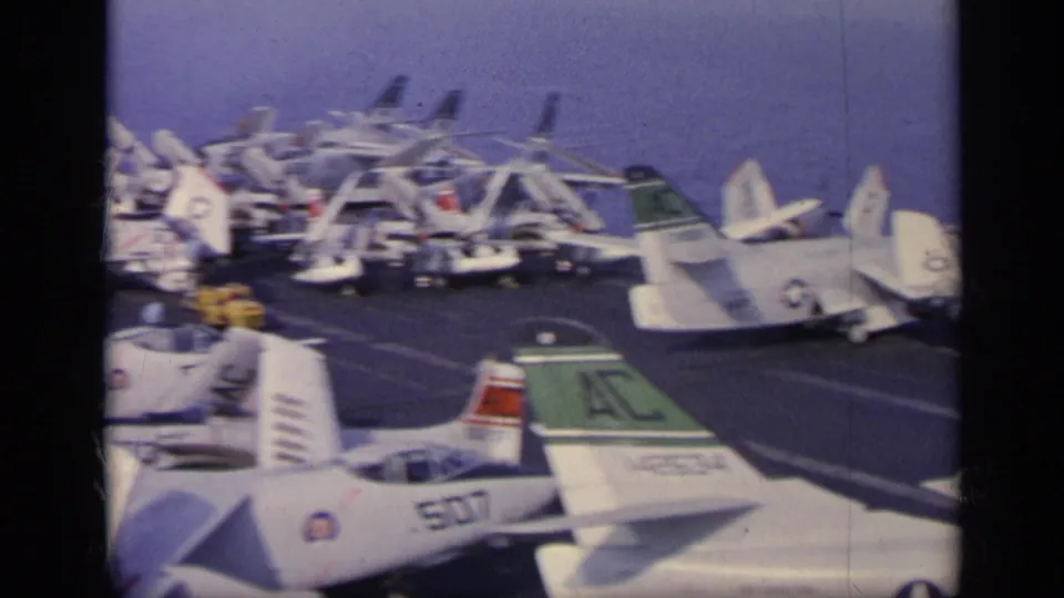 1962 U.S. Navy carrier deck near Italy showing rows of parked jets, visible tail codes, and crew working between aircraft.