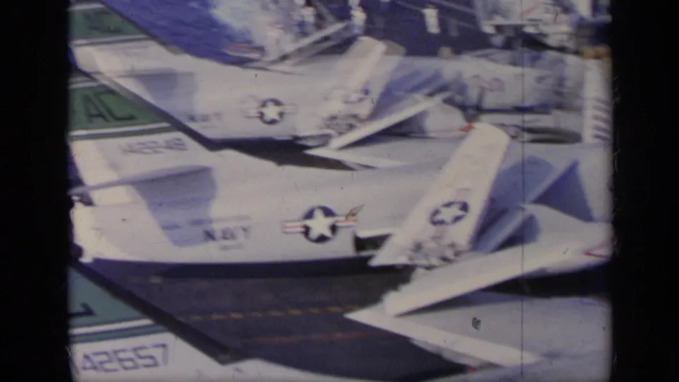 1962 U.S. Navy carrier-deck view near Italy with overlapping parked aircraft, tail numbers, insignia, and open water beyond.