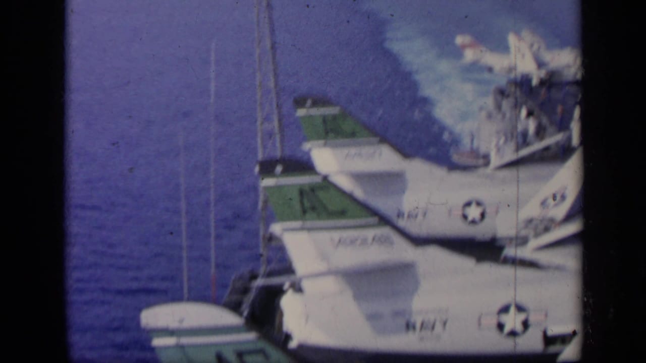 Close view of carrier deck aircraft with Navy markings beside blue water.