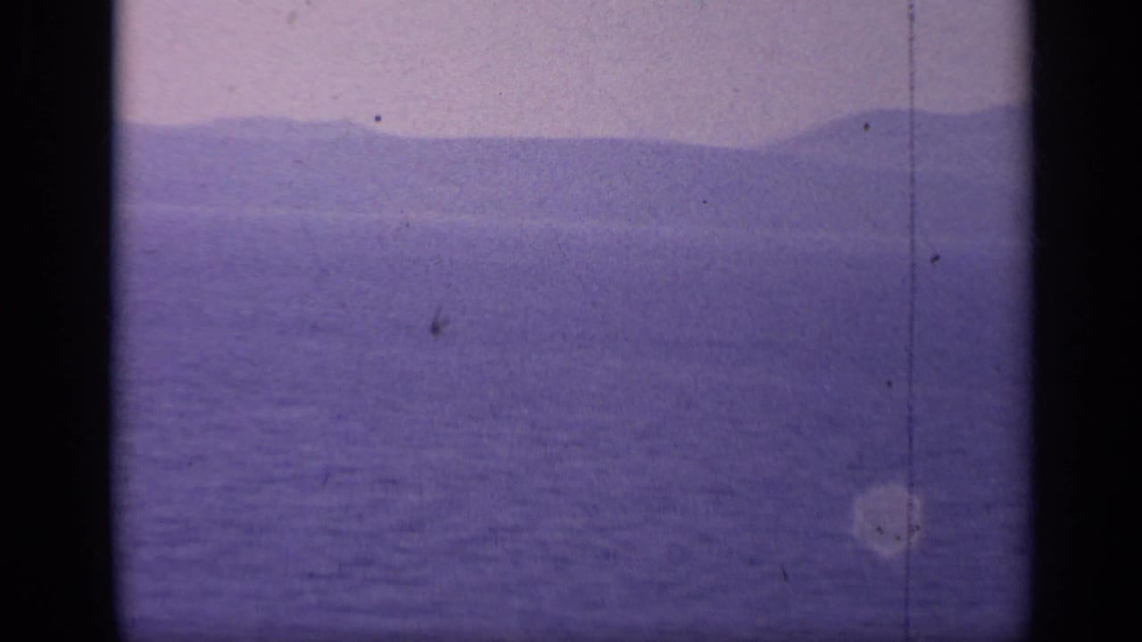 Purple-shifted sea and distant mountains with no ship clearly visible.