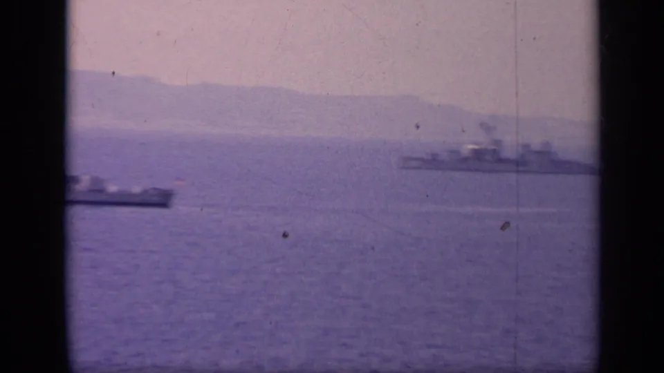1962 Italy 8mm frame showing distant vessels on purple-shifted water, with a soft mountain coastline and visible film wear.